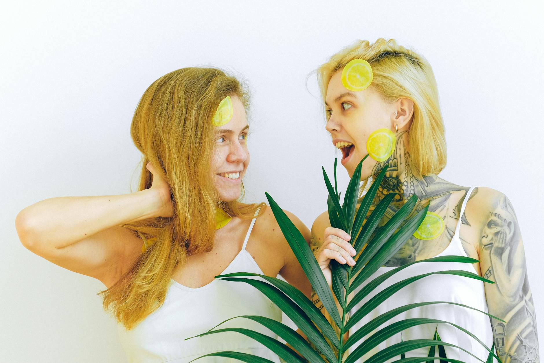 Two women smiling together with lemon slices indoors, expressing joy and playfulness.
