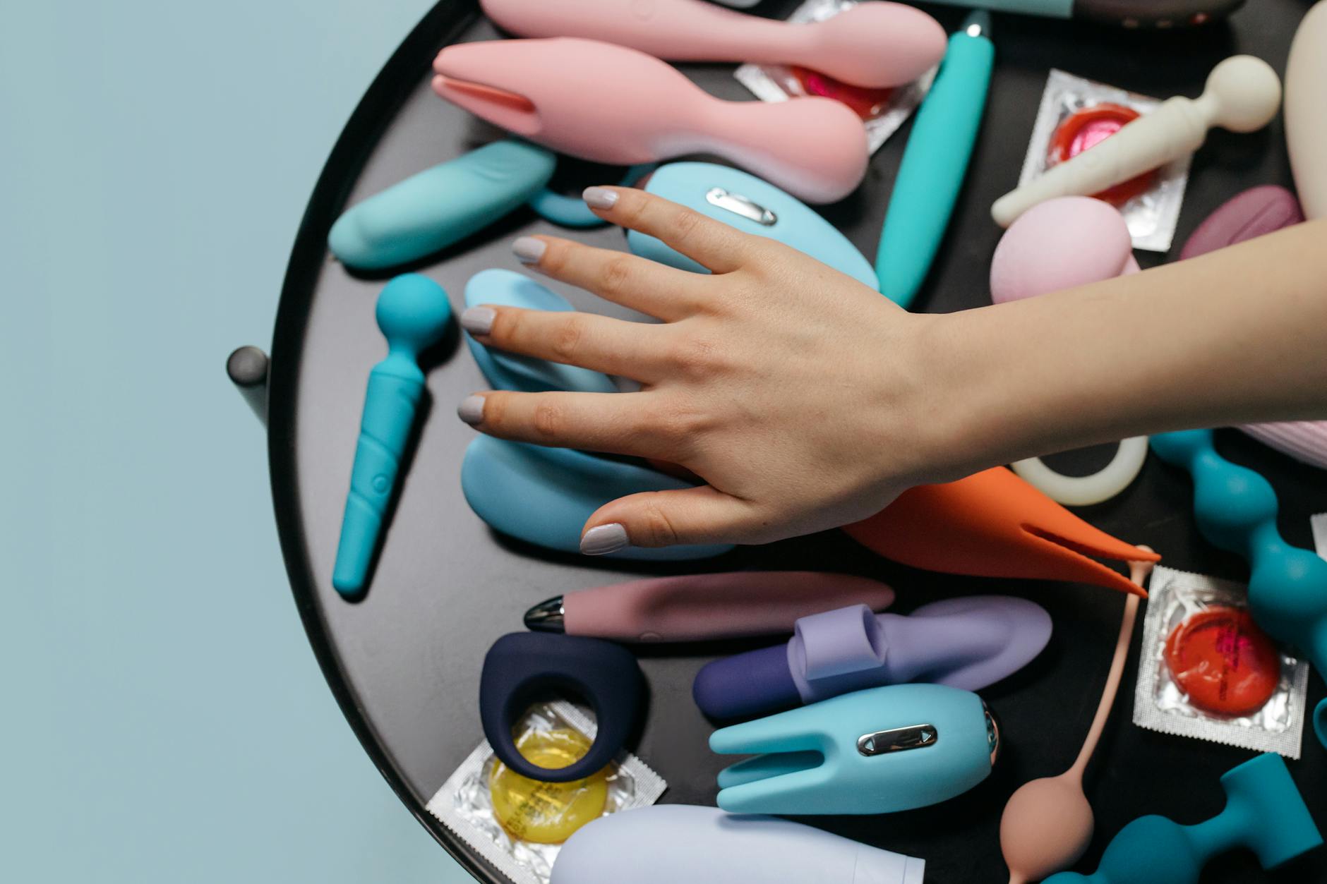 Person holding blue and pink silicone vibrators, considering safety and sensitivity