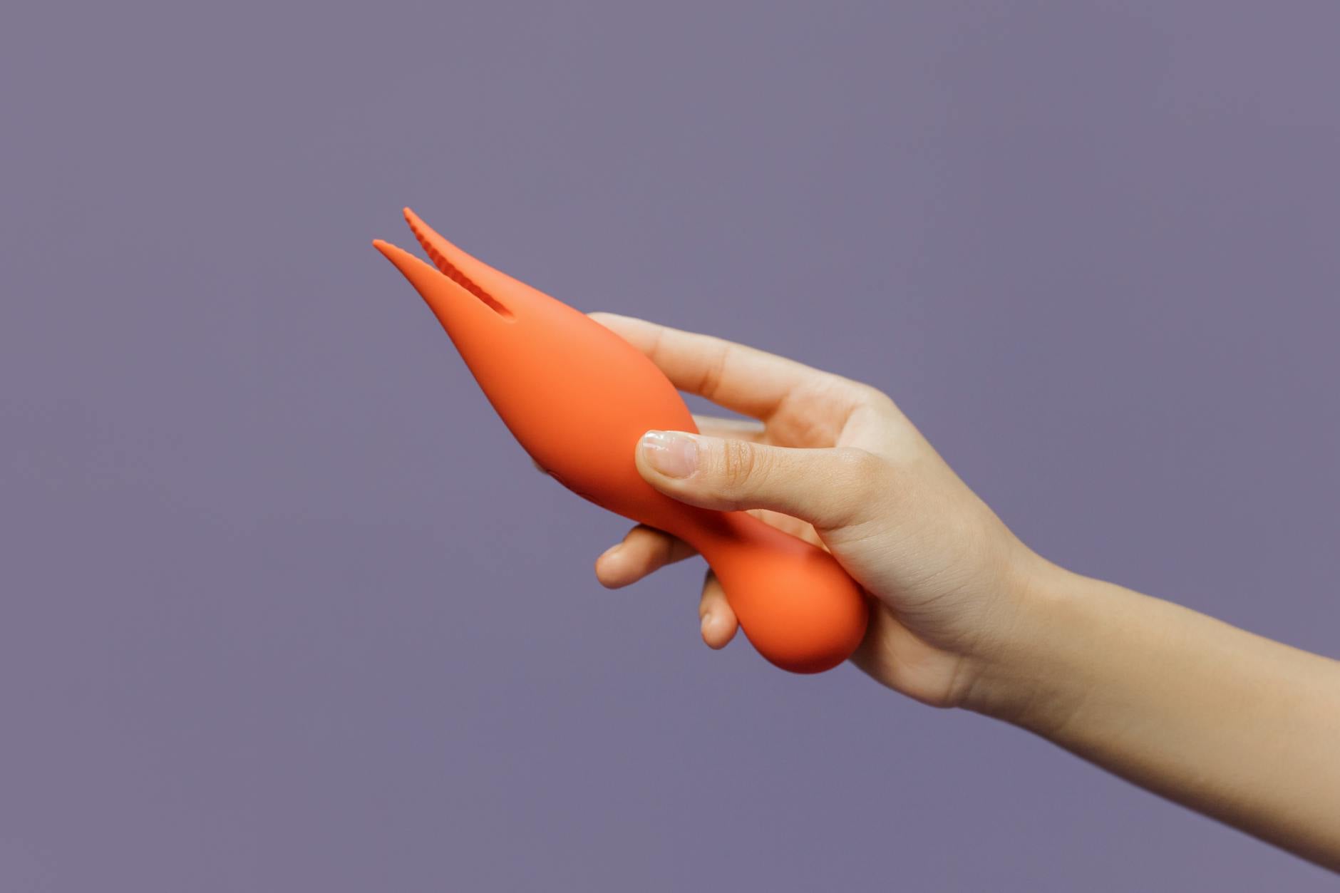 A hand holding a lemon clitoral vibrator against a minimalist purple backdrop