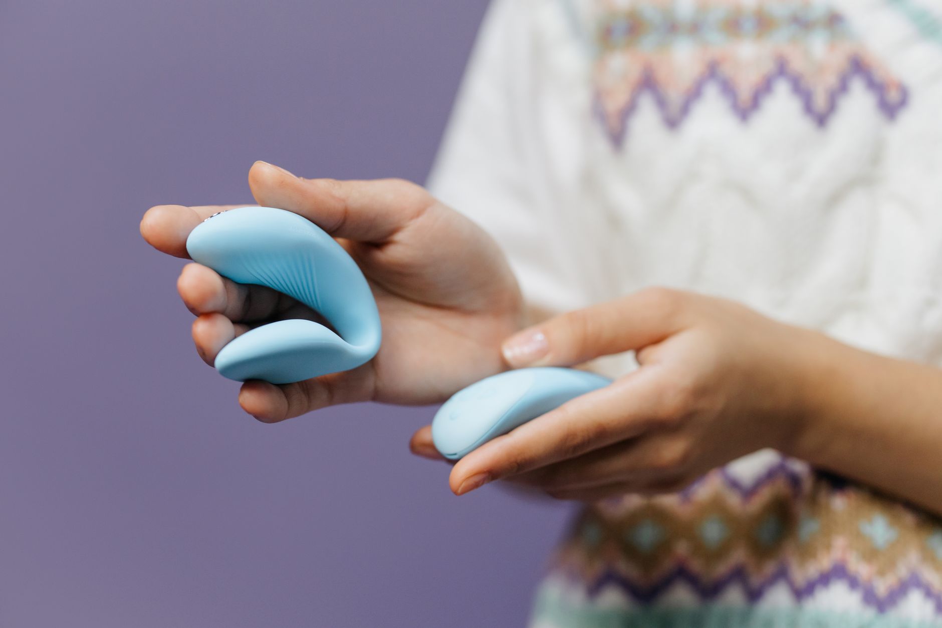 Close-up of hands holding a sleek blue vibrator, illustrating device control and settings.