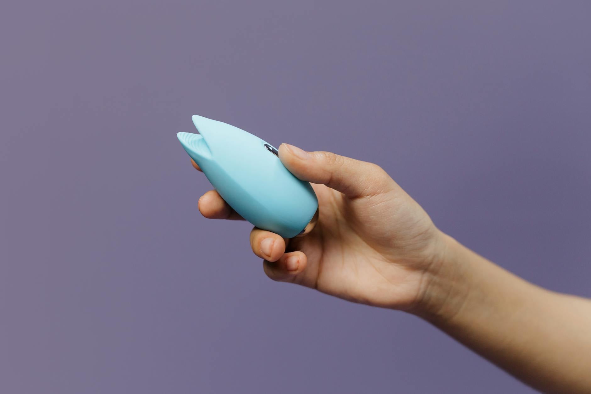 A lemon silicone vibrator held in hand against a purple background, showcasing innovative clitoral stimulation design
