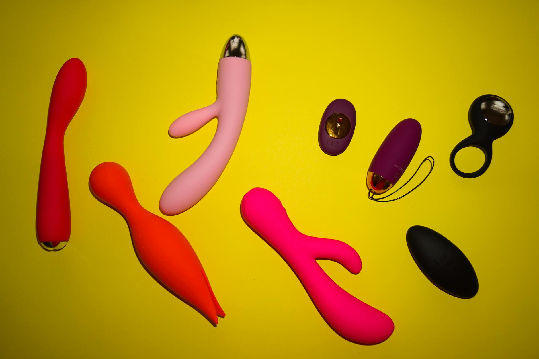 Colorful clitoral vibrators and sexual wellness toys arranged on a bright yellow surface